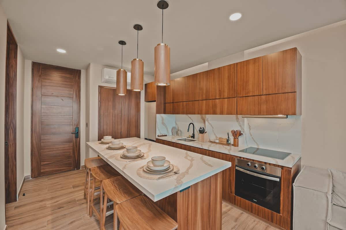 Contemporary kitchen with dark wood cabinetry, white marble countertops and backsplash, a long island with bar stools, and integrated appliances including an oven and electric stovetop.