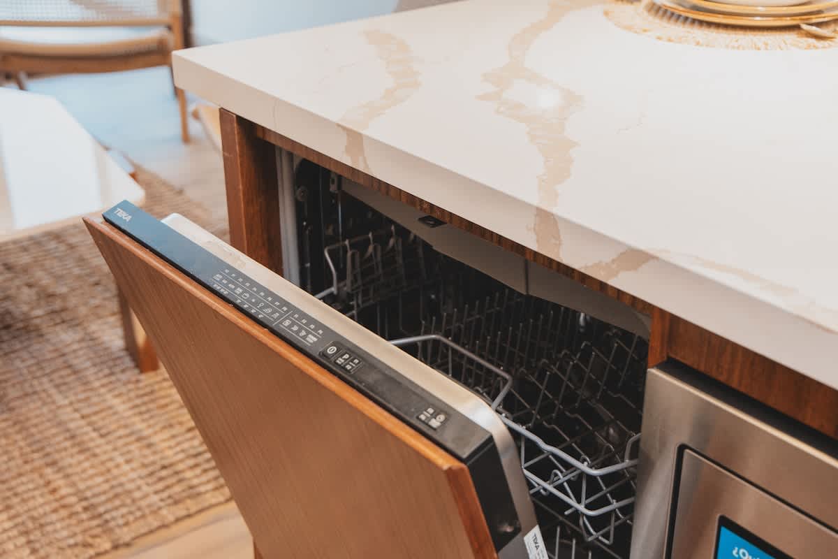 Close-up view of a modern kitchen with a partially open integrated dishwasher, featuring a wood panel door and a white and grey veined stone countertop, blending seamlessly with the cabinetry.