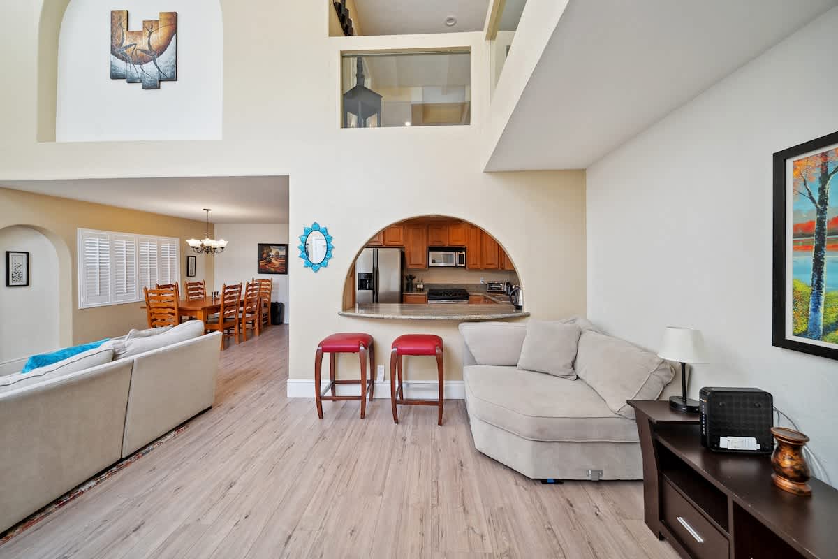 An open-concept living area flows into the dining space and kitchen, highlighted by an arched pass-through window to the kitchen. A cozy chaise lounge and two red bar stools provide additional seating.