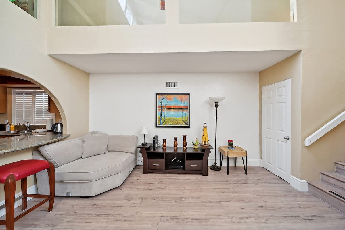 Another perspective of the living room highlights a comfortable chaise lounge, a media console adorned with decorative items, and a modern floor lamp. A white door and a staircase are visible on the right, beneath a large landscape painting.