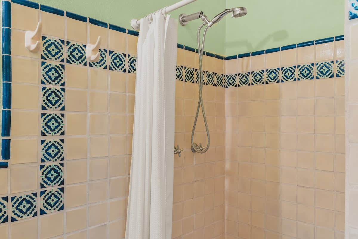A vibrant shower stall features light peach square tiles with a decorative blue and white patterned border, complemented by a light green wall and a simple white shower curtain.