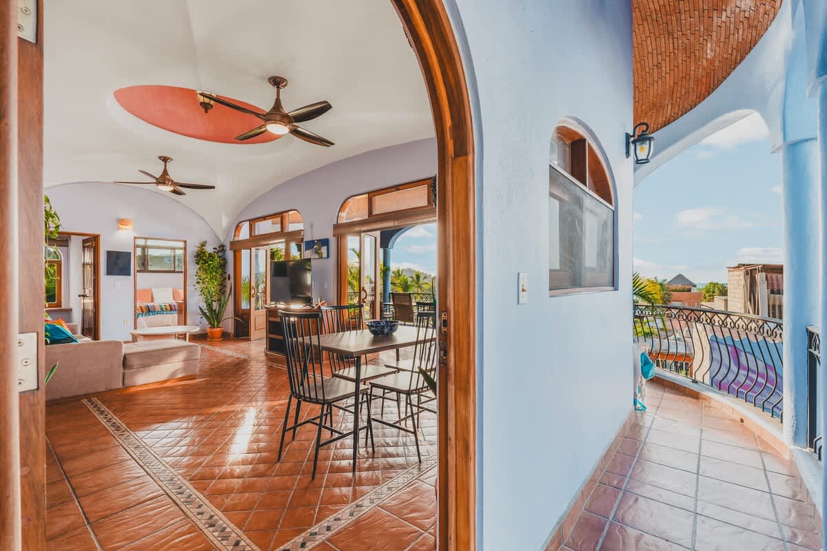 A wide arched entryway leading into an open-concept living and dining area with terracotta tiled floors, ceiling fans, and a view of the outdoor balcony through large glass doors.