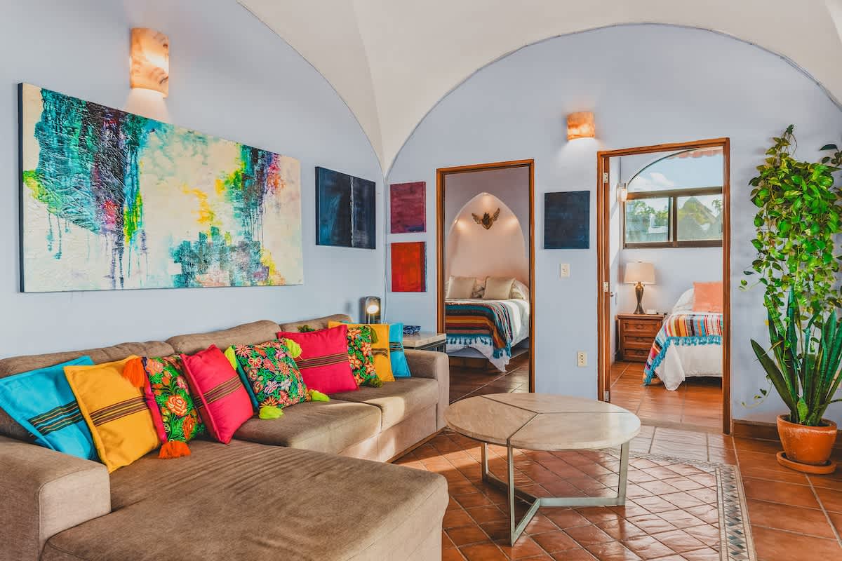 Another wide shot of the living room, highlighting the light blue walls, vaulted ceiling, and the arrangement of the sectional sofa, coffee table, and multiple doorways leading to bedrooms.
