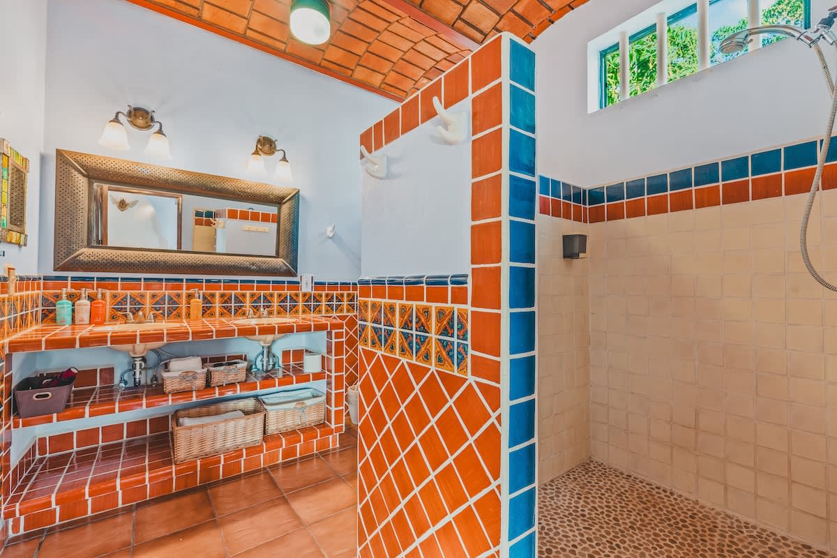 Vibrant bathroom featuring a double vanity with orange and blue tiled countertops and backsplash, a large mirror, and an open shower area with matching tiles and a pebble floor.