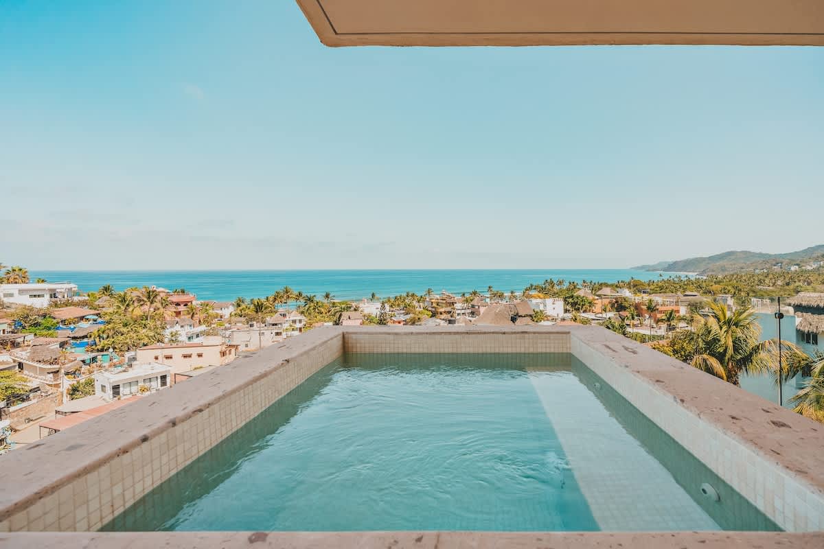 A rectangular hot tub on a tiled outdoor deck provides a refreshing soak with a panoramic backdrop of the ocean and a vibrant coastal town.