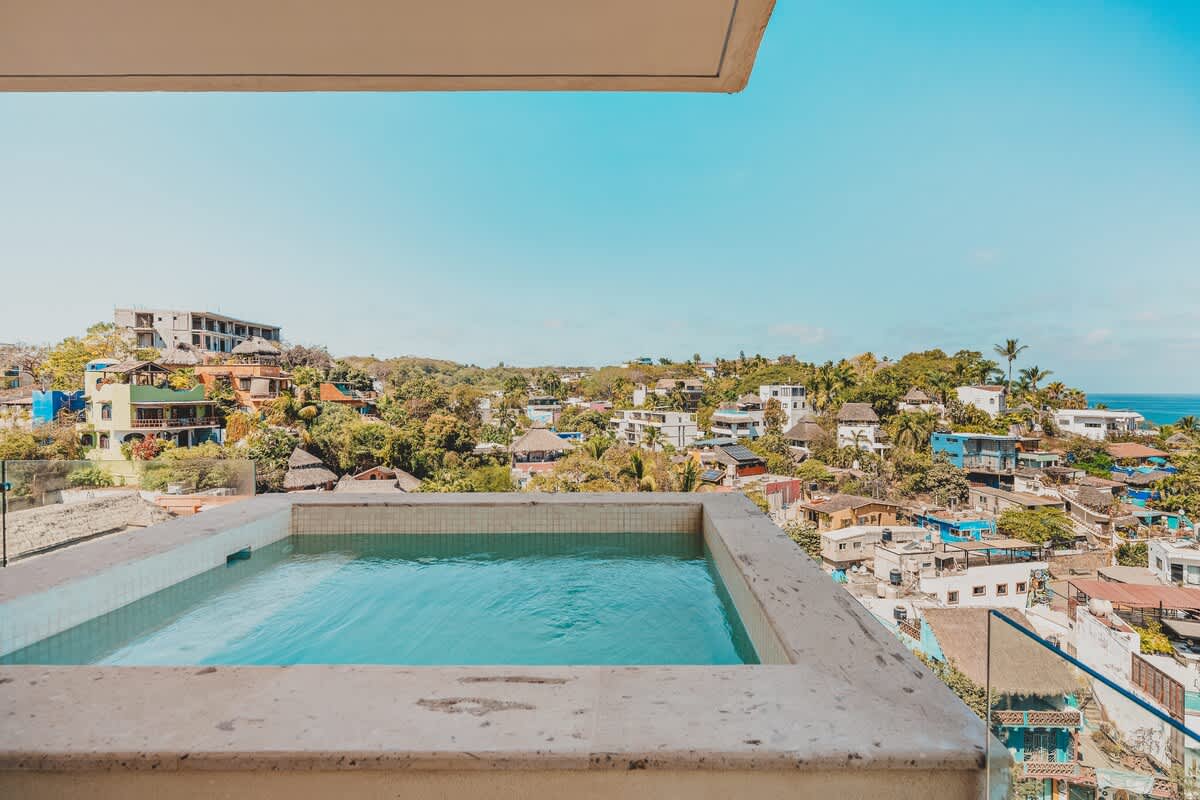 An elevated hot tub on a beige tiled terrace offers a serene spot with a wide view of a densely built coastal town and the distant horizon.