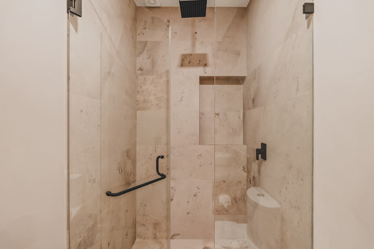 A sleek walk-in shower with light beige marble-patterned tiles, a black rain shower head, and a clear glass enclosure. Built-in niches provide convenient storage for toiletries, enhancing the modern and functional design.
