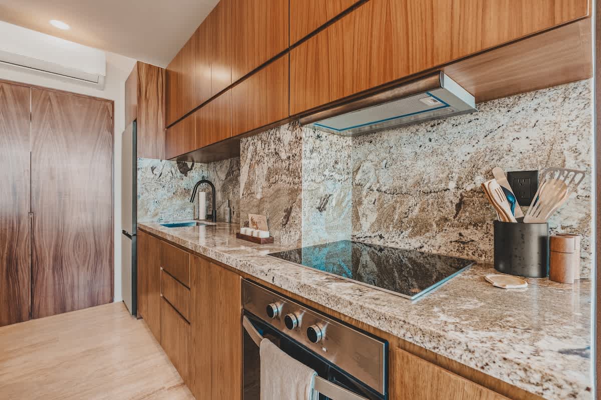 Detailed view of the modern kitchen counter with a built-in electric cooktop, sink, and a striking granite backsplash, surrounded by light wood cabinetry.
