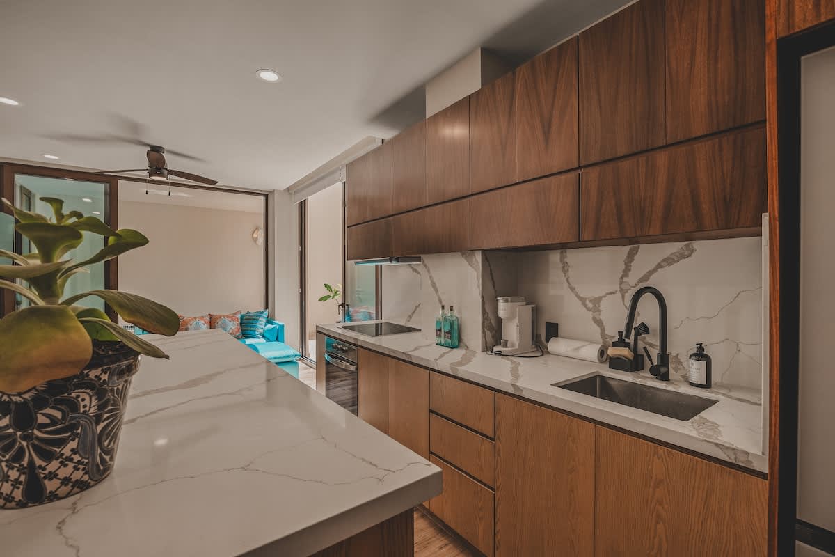 A contemporary kitchen boasts dark wood upper cabinets and light wood lower cabinets, complemented by white marble countertops and backsplash, featuring a black sink and faucet, and a built-in stovetop.