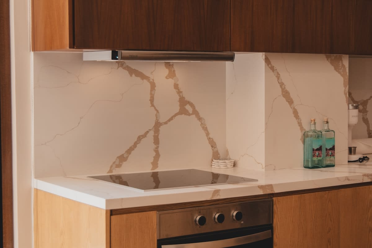Modern kitchen with white marble-patterned quartz countertops and backsplash, featuring a sleek black induction cooktop and a stainless steel range hood.