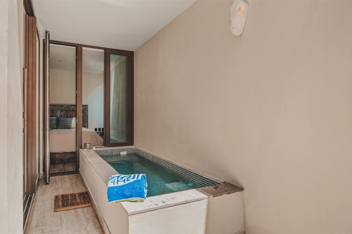 Inviting indoor plunge pool with blue mosaic tiles, set in a bright, minimalist space with light-colored walls and wood-look flooring. A blue and white towel is draped over the edge, ready for use.