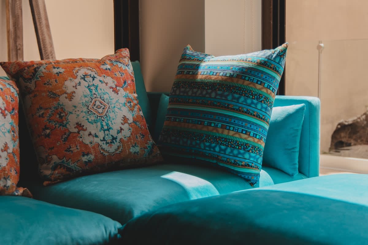 Close-up view of decorative pillows on a vibrant turquoise sofa, featuring intricate patterns in shades of orange, blue, and teal, adding a pop of color and texture to the living space.