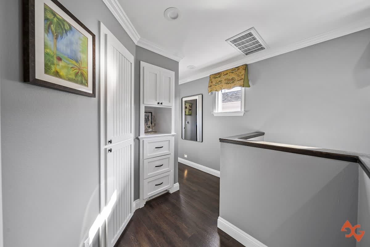 Bright hallway with light grey walls, dark wood flooring, a built-in white cabinet with drawers, and a small window, leading to a staircase with a dark wood railing.