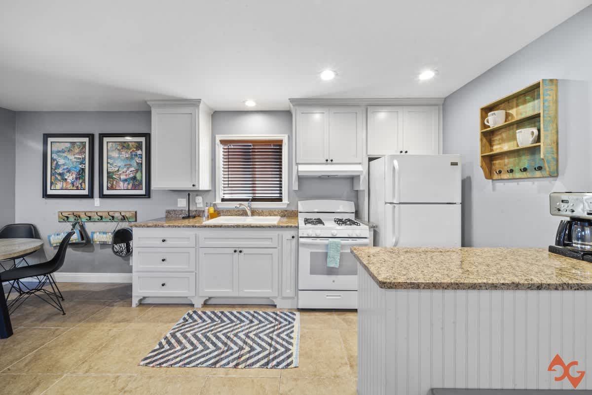 Bright kitchen featuring white shaker cabinets, speckled granite countertops, and a white stove and refrigerator, complemented by a blue and white chevron rug on light tile flooring.