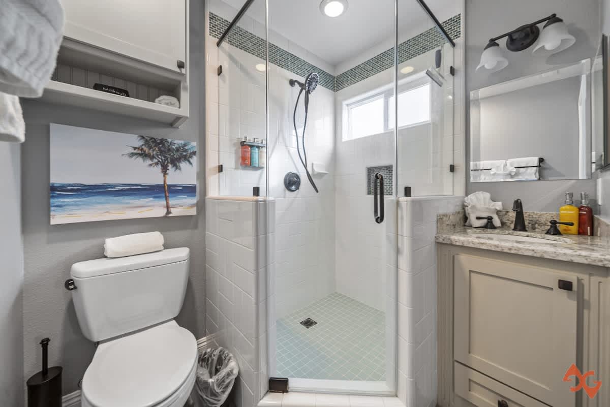 Bright bathroom featuring a glass-enclosed walk-in shower with white subway tiles, a white toilet, and a vanity with a light grey cabinet and a rectangular mirror.