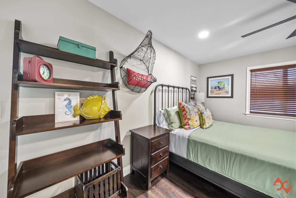 A bedroom with a black metal bed frame, a dark wood ladder bookshelf displaying decorative items, and a unique hanging wire basket, all contributing to a coastal theme.