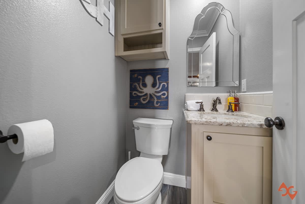 A compact bathroom with light gray walls, a white toilet, and a vanity with a light-colored countertop and a decorative mirror. A blue octopus wall art piece adds a nautical touch.