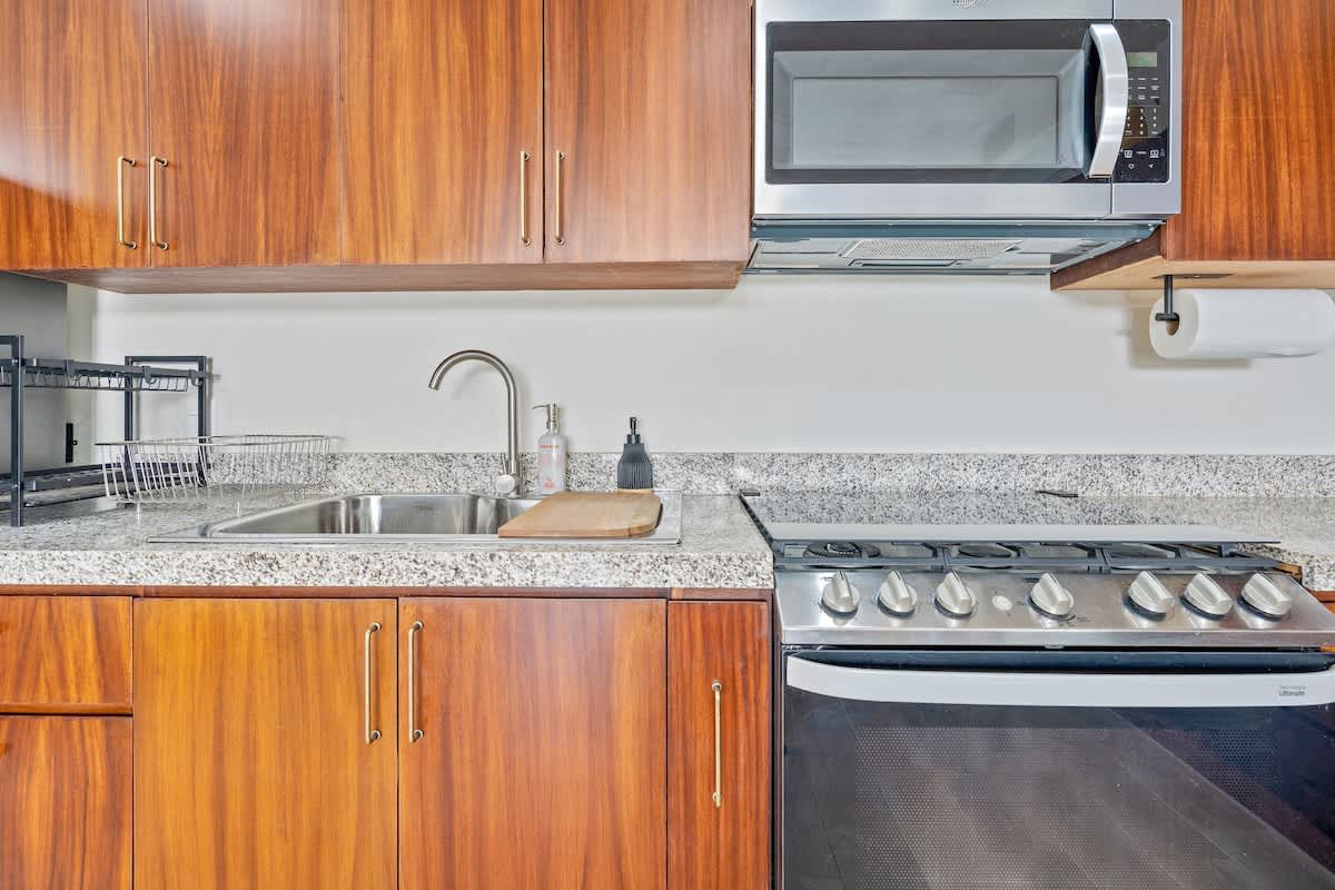 Close-up of the kitchen showing rich wood cabinetry, light granite countertops, a stainless steel sink, and a black and stainless steel oven/stove. A stainless steel microwave is mounted above.