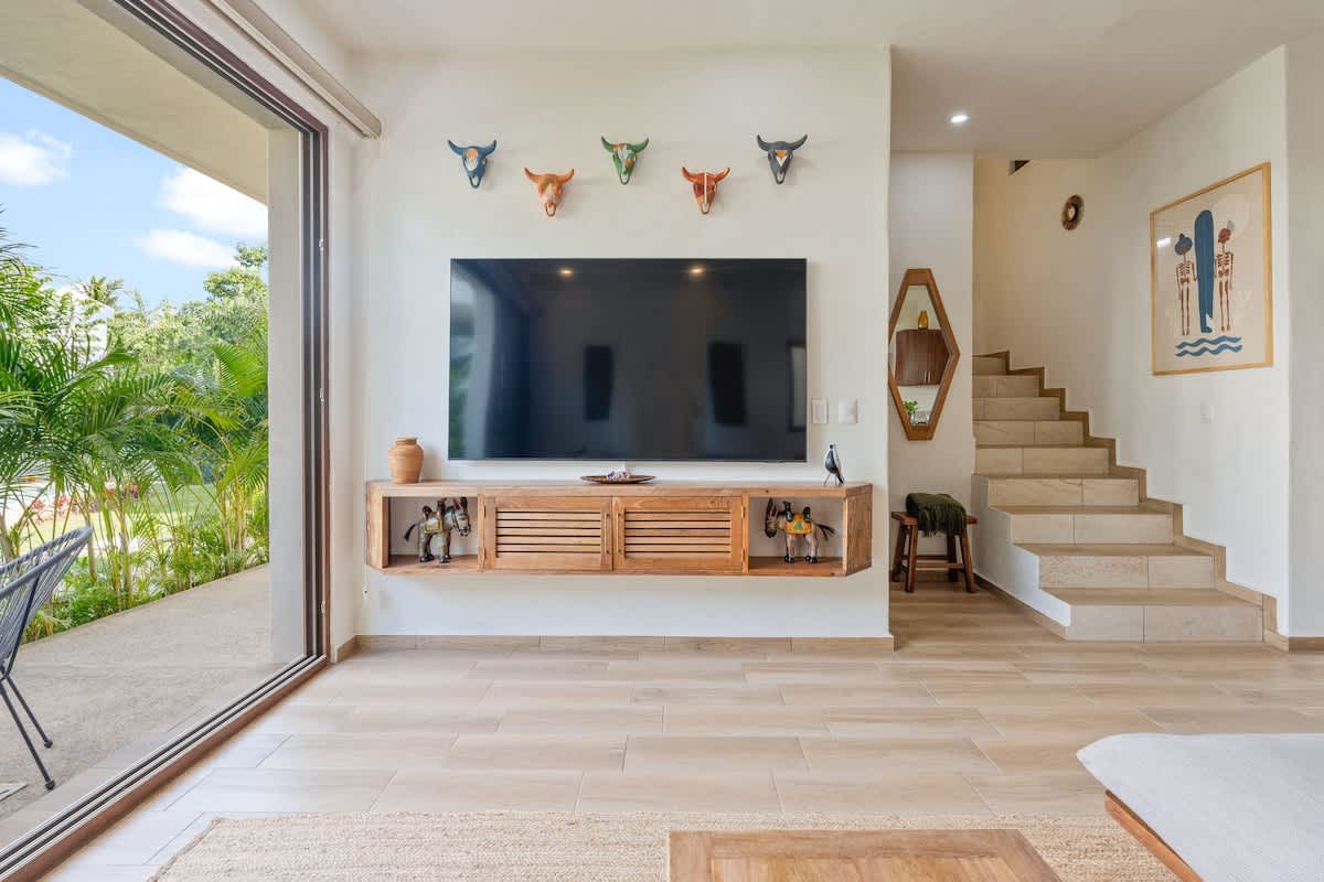Living room wall with a large wall-mounted flat-screen TV above a floating wooden media console, next to expansive sliding glass doors and a staircase leading to the upper level.