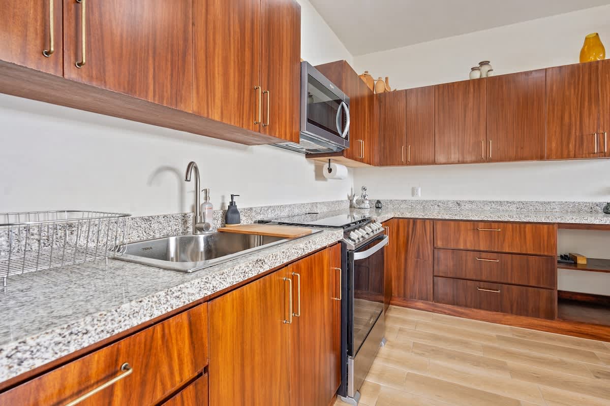 Modern kitchen with rich wood cabinetry, light granite countertops, a stainless steel sink, and a black and stainless steel oven/stove. A microwave is mounted above the stove.