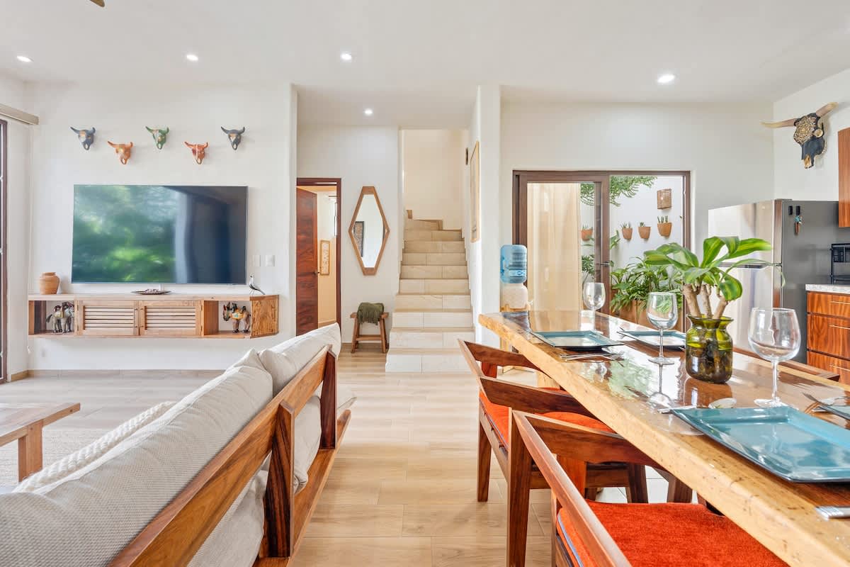 Expansive open-concept living space showcasing the comfortable sectional sofa, the live-edge dining table, and the modern kitchen, with a staircase visible in the background leading to the upper floor.