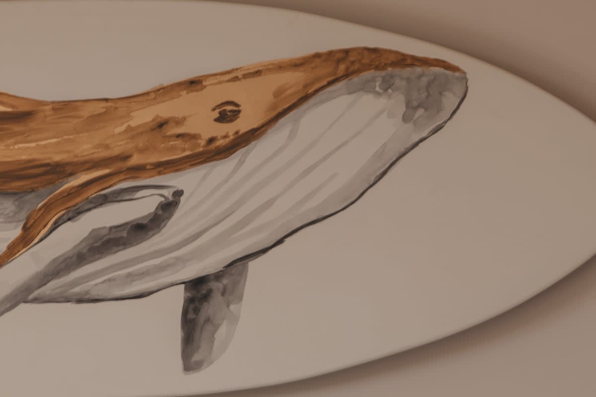 A close-up of a surfboard-shaped wall art piece features a watercolor painting of a brown and grey whale, adding a coastal touch to the decor.