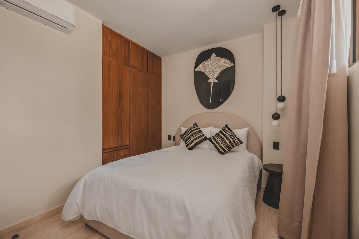 Full view of bedroom-2 with a queen bed, a striking stingray artwork, and a built-in wooden wardrobe, illuminated by modern pendant lights.