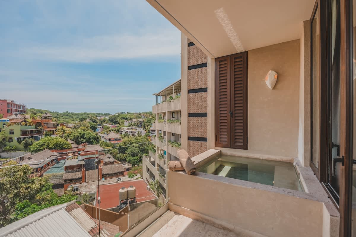 Private balcony featuring a small built-in plunge pool or hot tub, offering expansive views of the surrounding town and verdant hills under a clear blue sky.