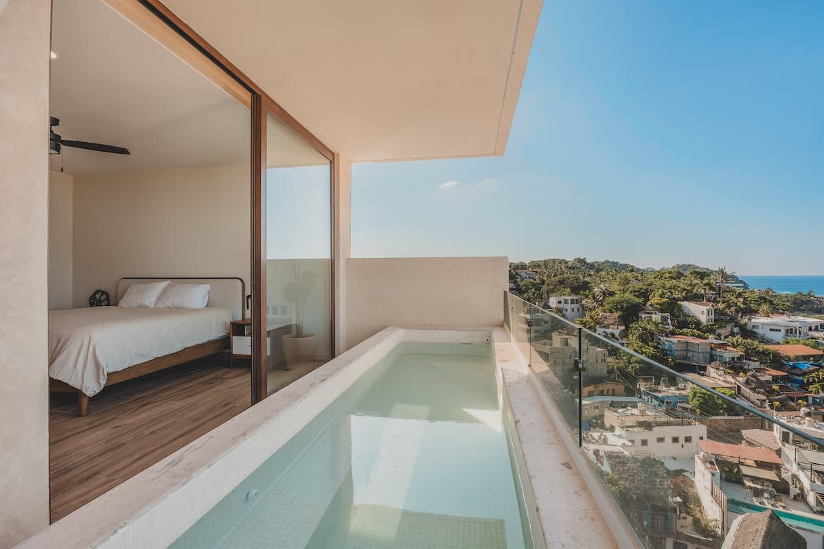 Serene bedroom with a queen-sized bed and wood flooring, featuring direct sliding glass door access to a private balcony with a plunge pool and stunning ocean views.