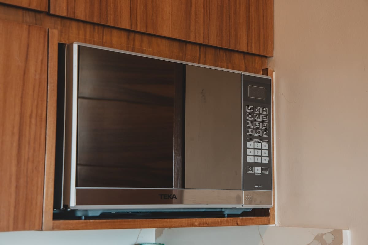 A sleek silver and black Teka microwave oven is neatly integrated into the warm wooden cabinetry of the kitchen. Its digital display and control panel are visible, suggesting modern functionality.
