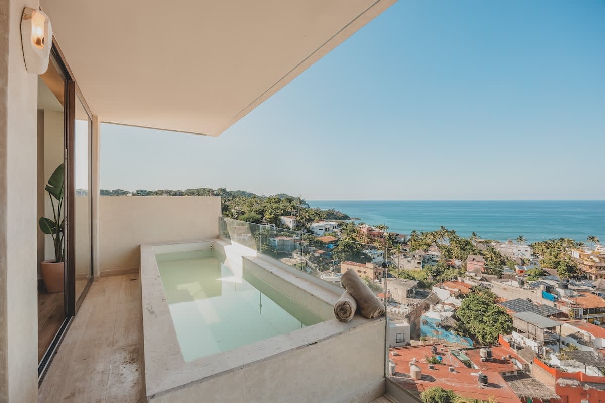Inviting plunge pool on a private balcony, offering breathtaking views of the ocean and the bustling town below, with rolled towels placed neatly beside it.