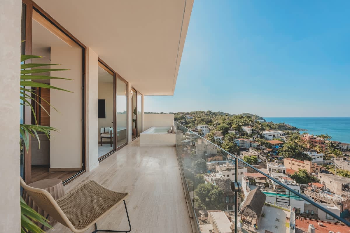 Expansive balcony featuring a private plunge pool and comfortable outdoor seating, all set against a stunning backdrop of the ocean and a sprawling coastal town.