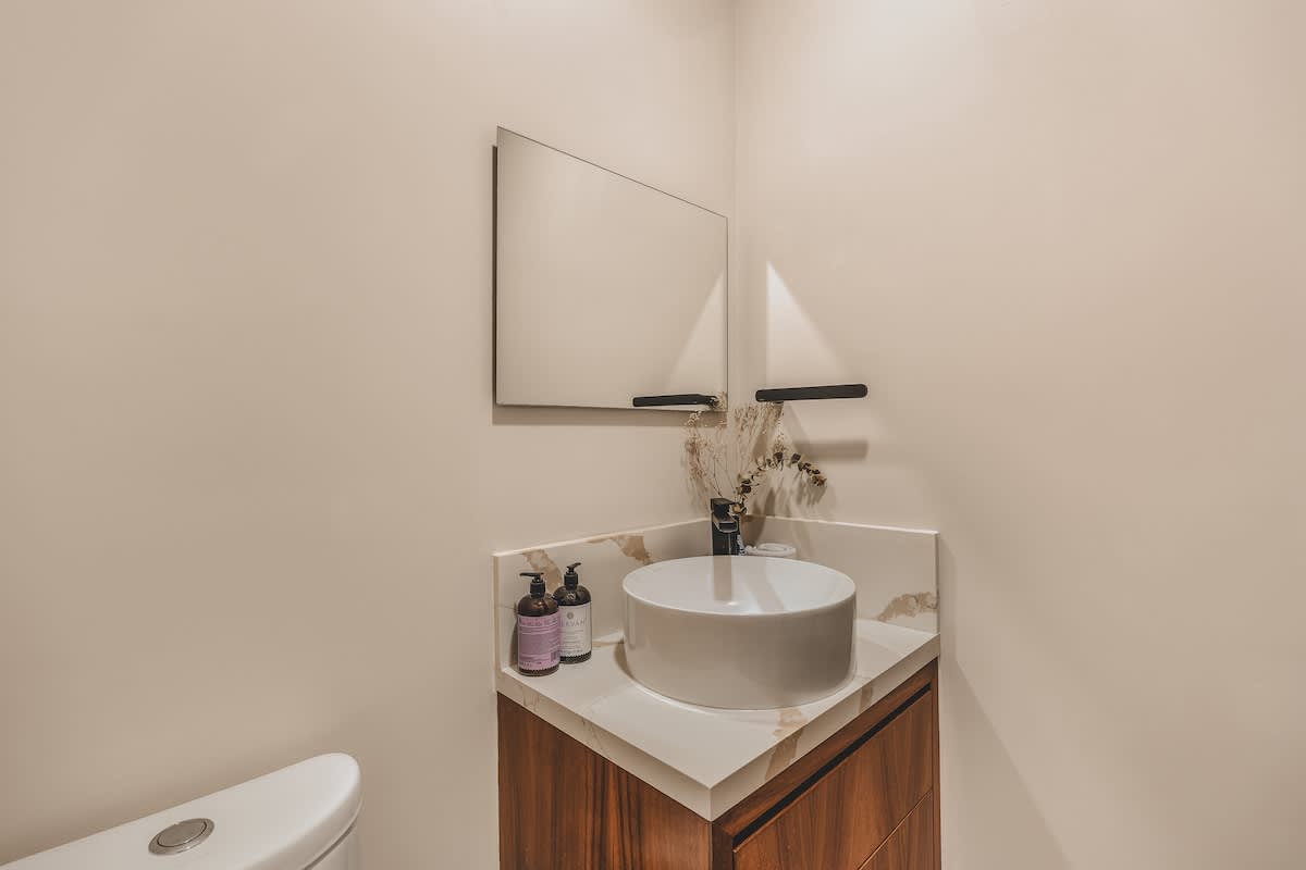 Modern half-bathroom featuring a corner vanity with a white vessel sink, a marble countertop, dark wood cabinetry, and a sleek rectangular mirror above, with a toilet partially visible.