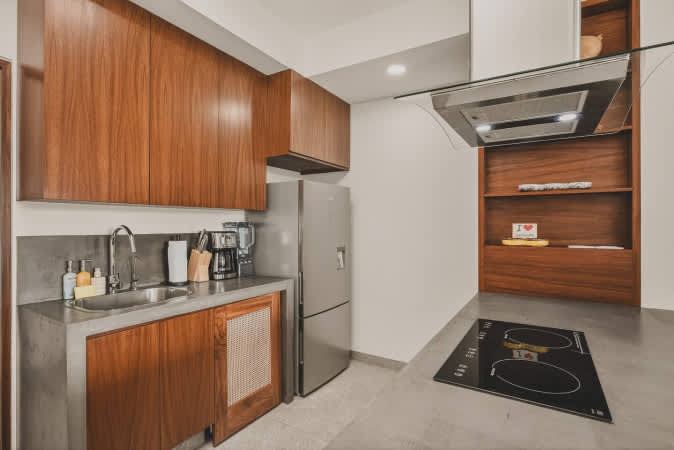 Detailed view of the modern kitchen featuring a robust concrete countertop, stainless steel sink, warm wooden cabinetry, and a stainless steel refrigerator. The induction cooktop on the island is ready for use.