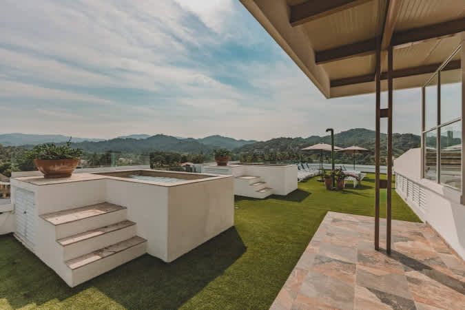 Rooftop deck featuring two built-in hot tubs with steps, artificial turf, and potted plants, offering panoramic views of distant mountains under a partly cloudy sky.