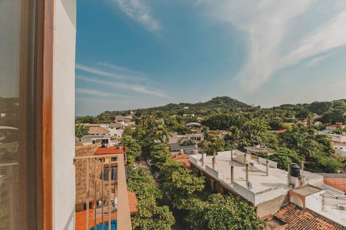 View from a balcony overlooking a residential area with various houses and abundant green trees, set against a backdrop of rolling hills and distant mountains.