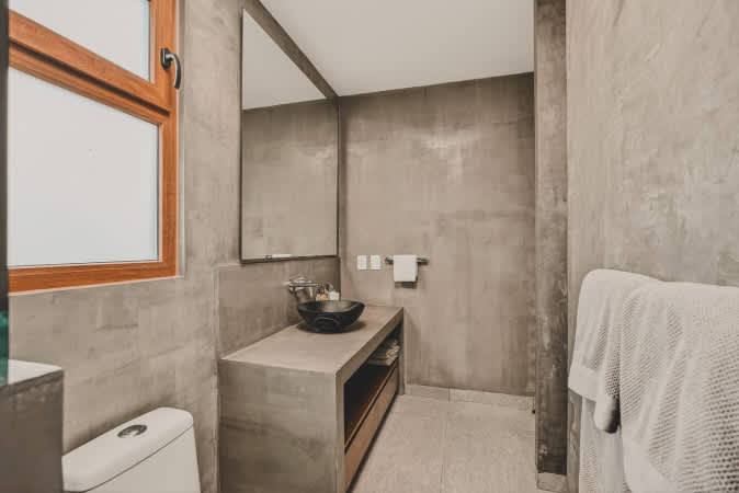 Contemporary bathroom featuring textured concrete walls and a matching vanity with a stylish black vessel sink. A large rectangular mirror hangs above, and a toilet is partially visible on the left.