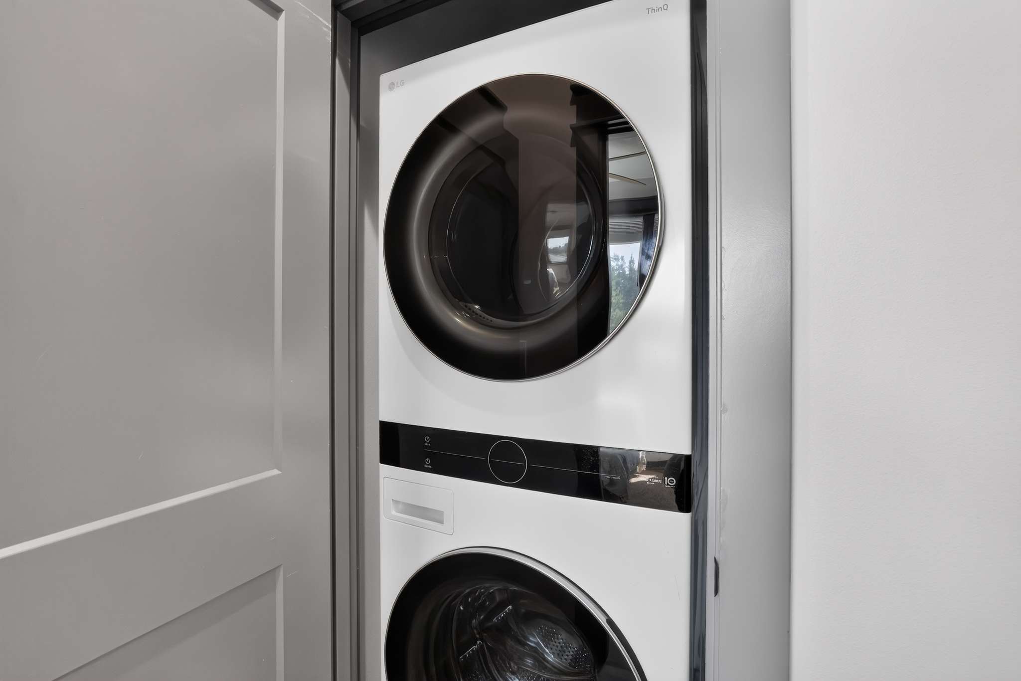 A modern white stacked LG ThinQ washer and dryer unit is neatly tucked into a closet space, featuring sleek black circular doors and digital controls, providing efficient laundry facilities.