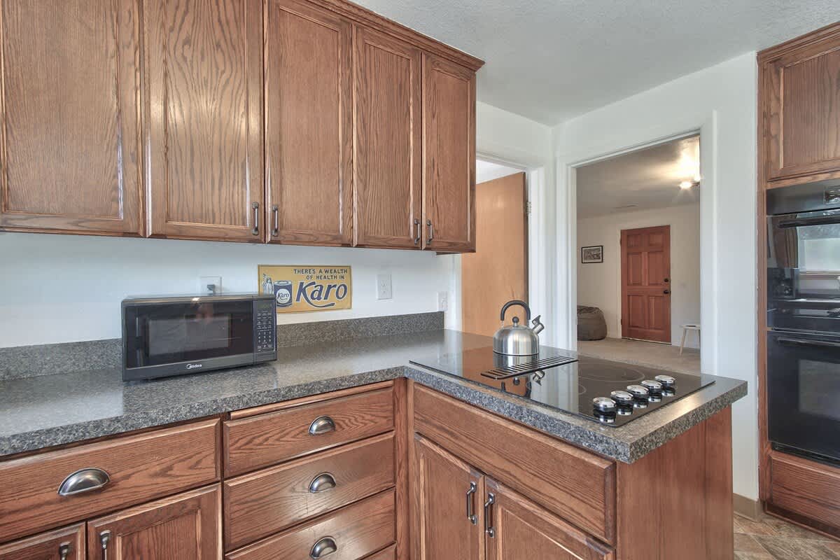 A section of the kitchen showcasing a black electric cooktop integrated into the dark countertop, with a black microwave oven on the adjacent counter. Dark wood cabinets line the walls, and a vintage-style sign adds a touch of decor.