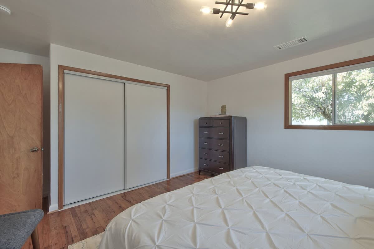 View of a bedroom showcasing a spacious closet with white sliding doors, a dark wood dresser, and a large bed with a white duvet, all set on rich hardwood floors.