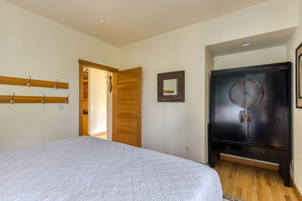 A different angle of bedroom-1 reveals light wood flooring and a striking black armoire with circular detailing. A wooden door leads to an adjacent room, and additional wooden coat racks adorn the wall.