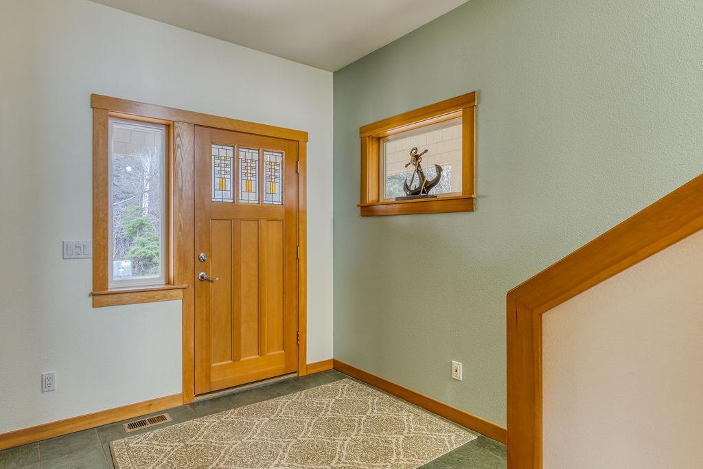 Welcoming foyer with a light wood front door featuring stained glass accents and side windows, set against light green and white walls. A decorative anchor sculpture is visible through an interior window.