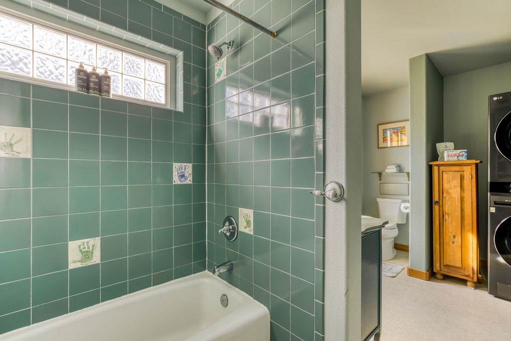 A close-up of the shower/tub combo in bathroom-1, featuring green square tiles, a white bathtub, and a small glass block window above the shower.