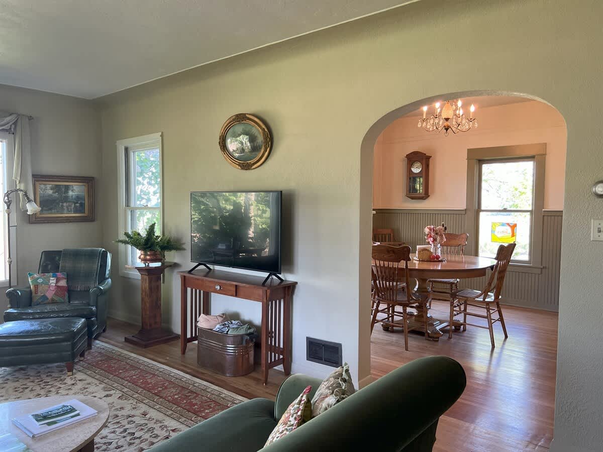 Spacious living room featuring a flat-screen TV on a wooden console, a comfortable armchair, and a sofa, with a patterned rug defining the space, and an arched opening leading to the dining area.