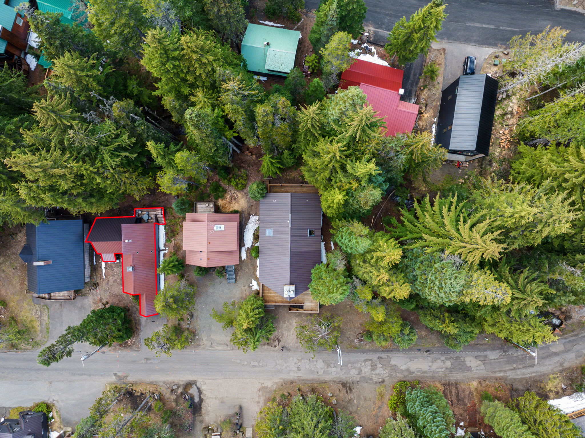 Aerial overhead view of multiple cabins and houses with colorful roofs nestled in a dense evergreen forest with a road.