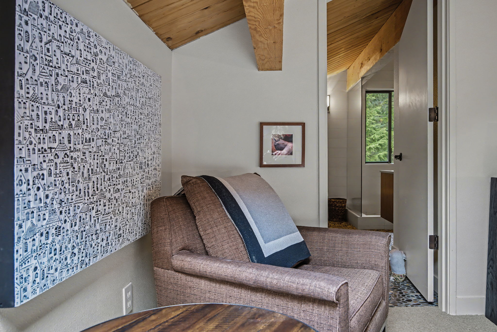 Grand living room with a towering stone fireplace as the focal point, flanked by two dark sofas. Floor-to-ceiling windows offer panoramic views of the surrounding forest and mountains.