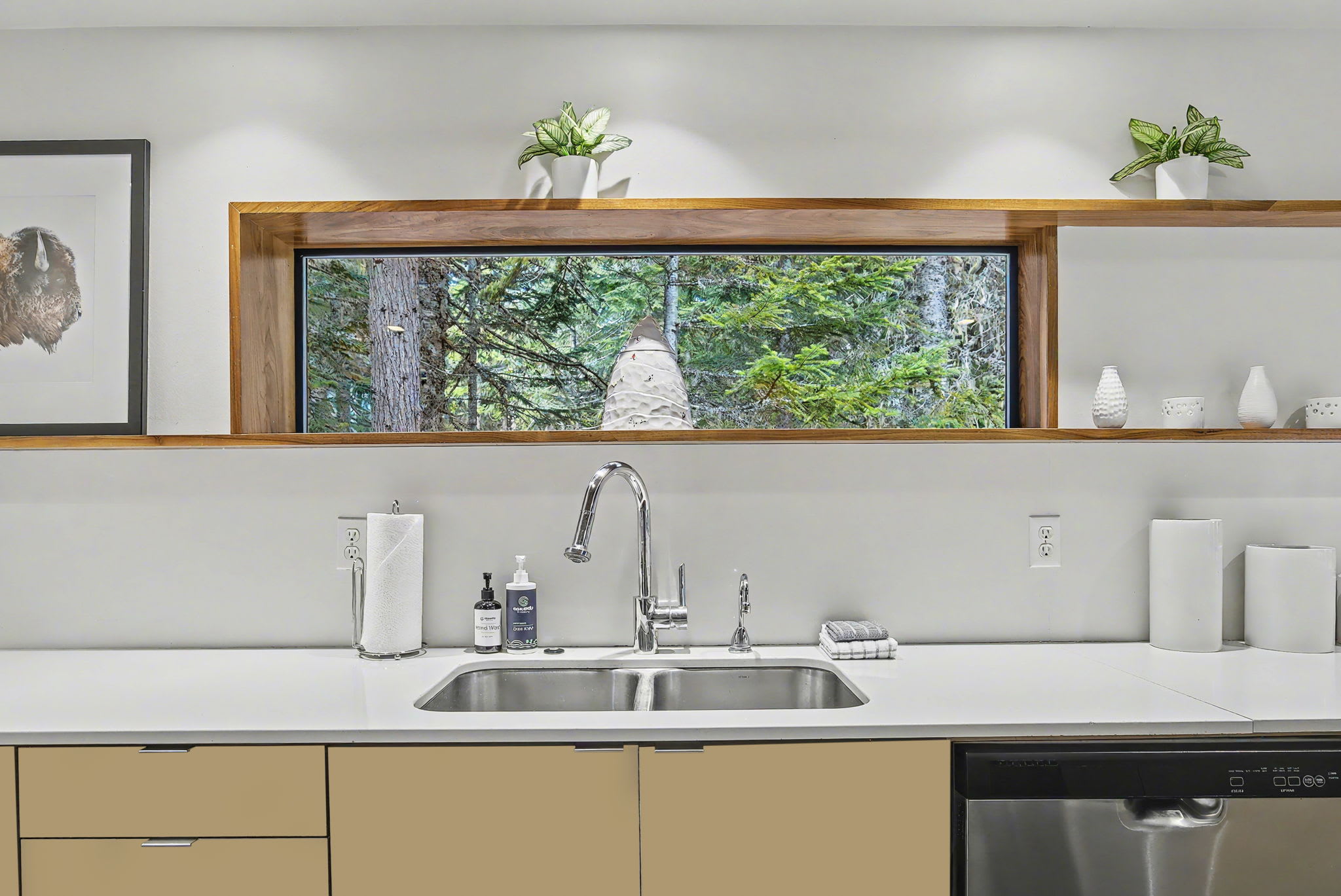 A wider view of the modern kitchen, showcasing a large stainless steel refrigerator and light cabinetry, with an open doorway leading to another area. Hardwood floors and a vaulted wooden ceiling maintain continuity with the rest of the house.