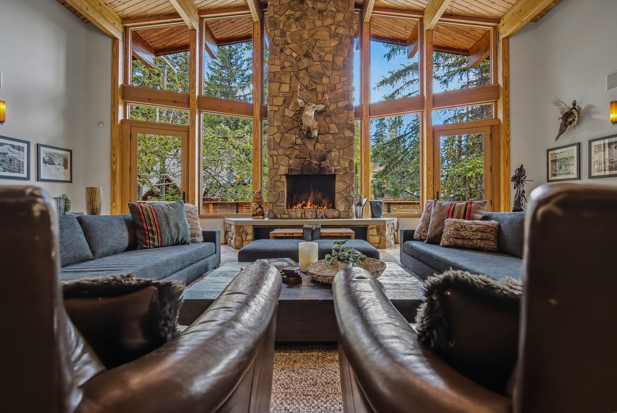 Open concept living area with a white bar counter and three modern bar stools, separating it from the main living space. A large window provides a picturesque view of the forest.