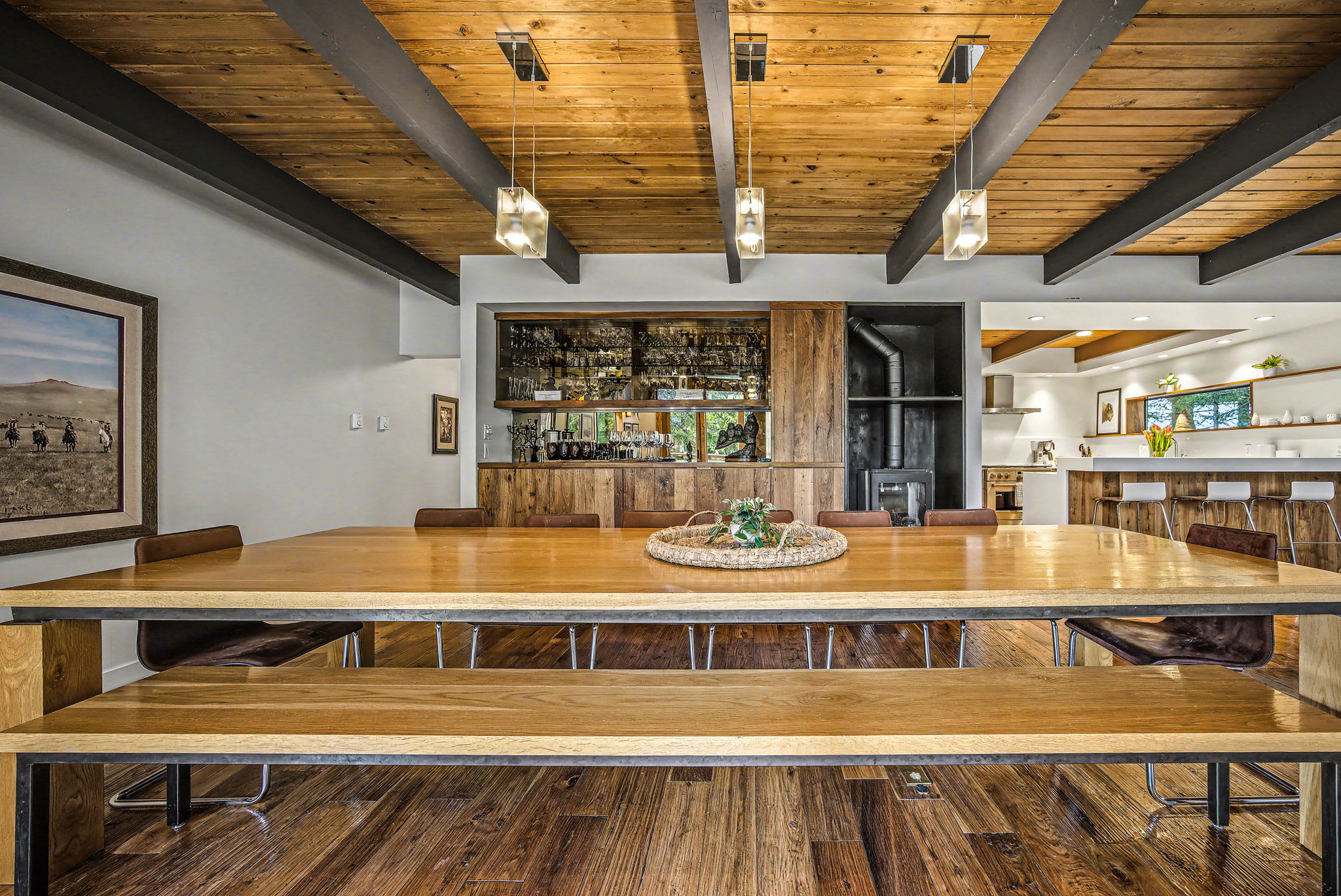 A spacious living room showcases a dark sectional sofa with plush pillows, hardwood floors, and a vaulted wooden ceiling. Animal mounts adorn the walls, and a built-in bar area with mirrored shelves is visible in the background.