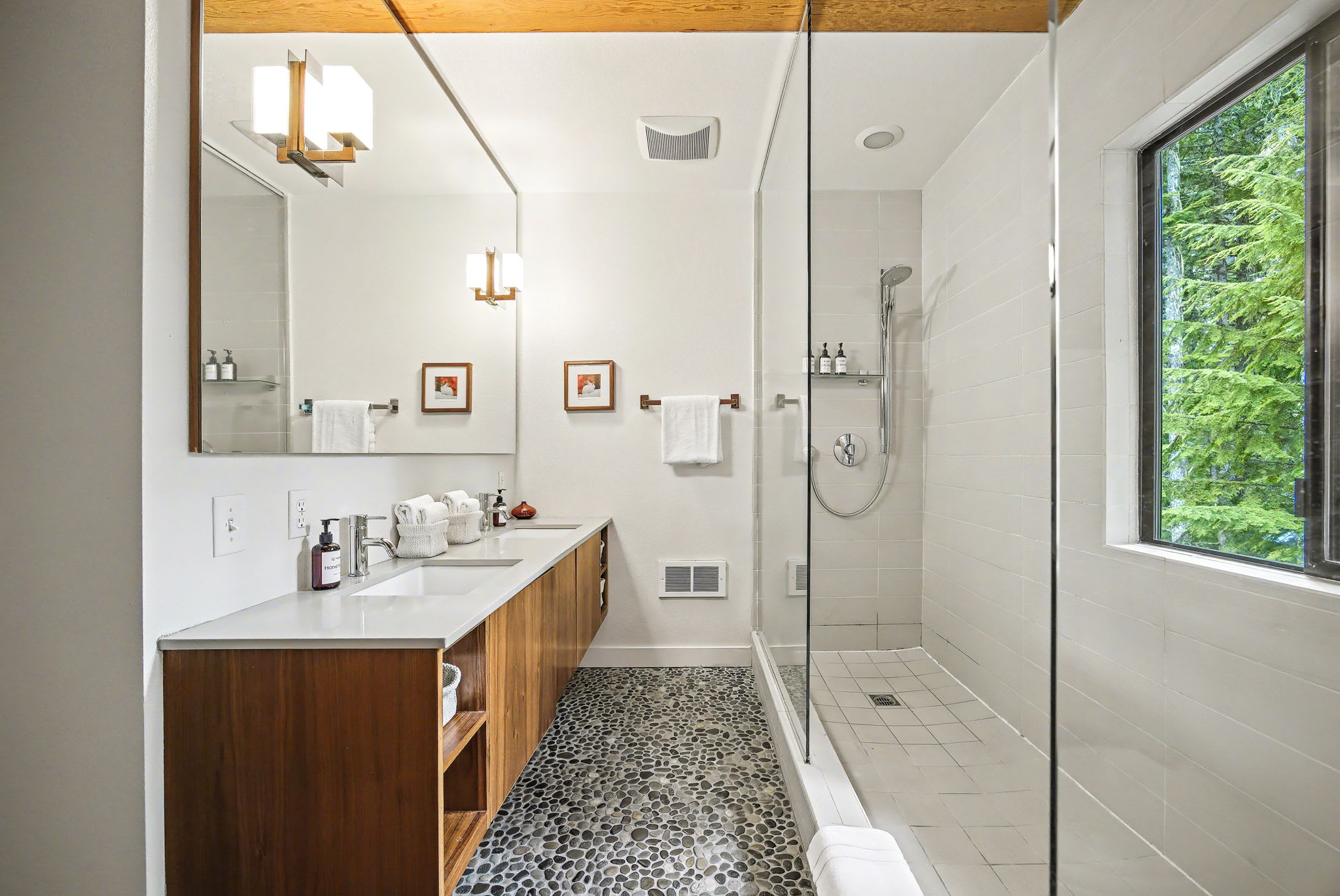 This bedroom view features a mid-century modern wooden dresser with multiple drawers, topped with decorative vases and a framed mirror. A large abstract painting leans against the wall, and a white door leads to another room, all under exposed wooden beams.